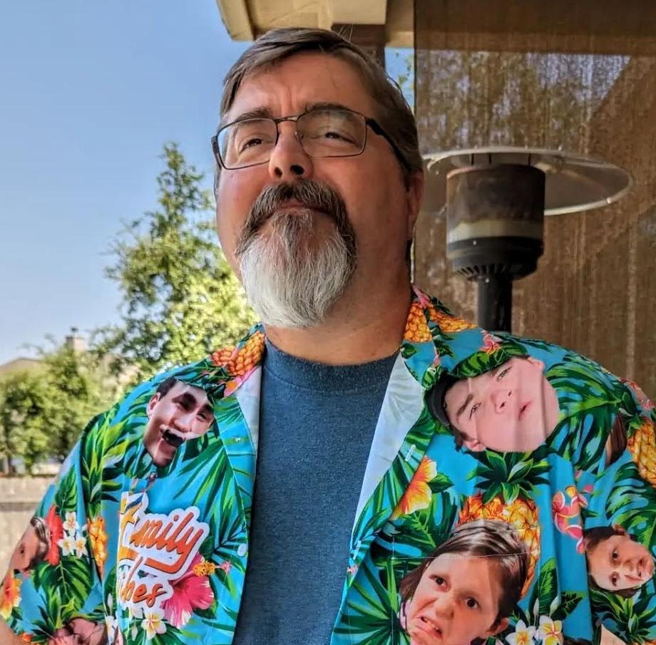 Ryan Thomas looking thoughtfully into the distance while wearing a quirky smile, and wearing an awesome shirt with his family on it.